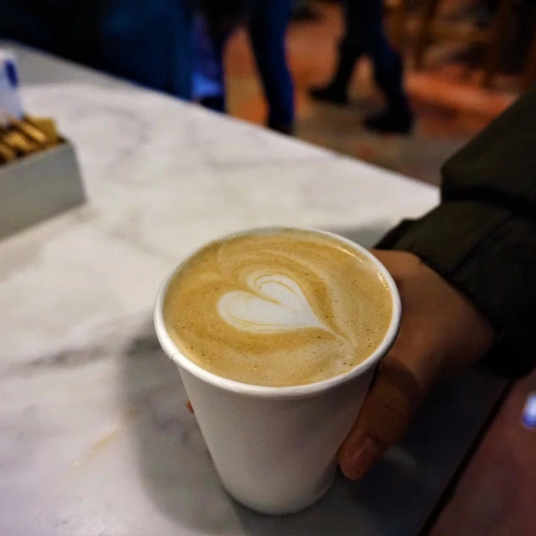 A hand holding a white cup of latte on marble — illustrative serving or coffee study