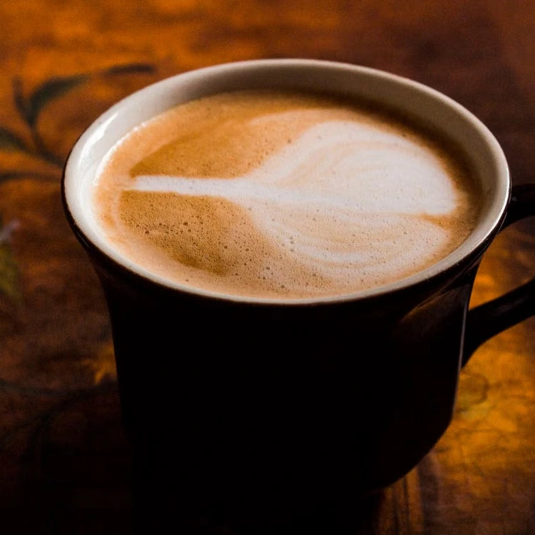 Latte in a dark ceramic cup on a warm wooden table — illustrative serving or coffee study